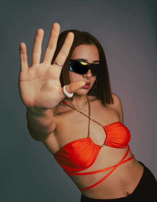 Artista con top rojo extendiendo la mano hacia la cámara
