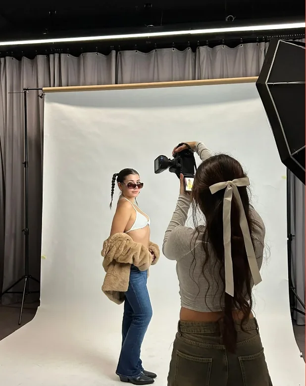Sesión en estudio: fotógrafa dirigiendo a una modelo sobre fondo blanco